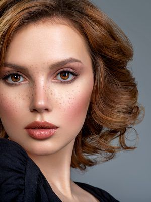 Beautiful brown haired with stylish short hairstyle. Woman with a  curly hair. Beautiful young woman with freckles on face.  Closeup portrait of an attractive girl  with a brown makeup.