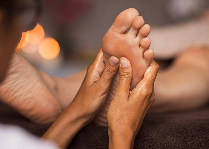 Closeup of masseuse doing foot reflexology to woman at spa. Therapist hands doing foot massage at wellness center. Woman receiving a feet massage at health spa.